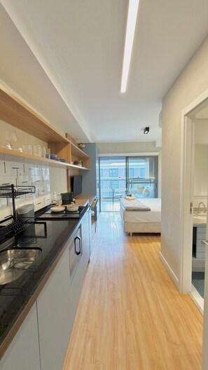 Una cocina moderna con una isla central, un comedor con mesa y sillas, y un dormitorio con cama y ventana.