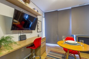 A modern dining area with a round table, red chairs, a television mounted on the wall, and a potted plant on the floor. - Innvista - AirBrooklin (São Paulo)