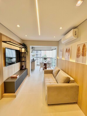 Una sala de estar moderna con un sofá, televisor y un comedor con sillas y una mesa.