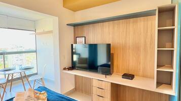 A modern hotel room with a bed, a TV, a desk, and a balcony with a table and chairs.