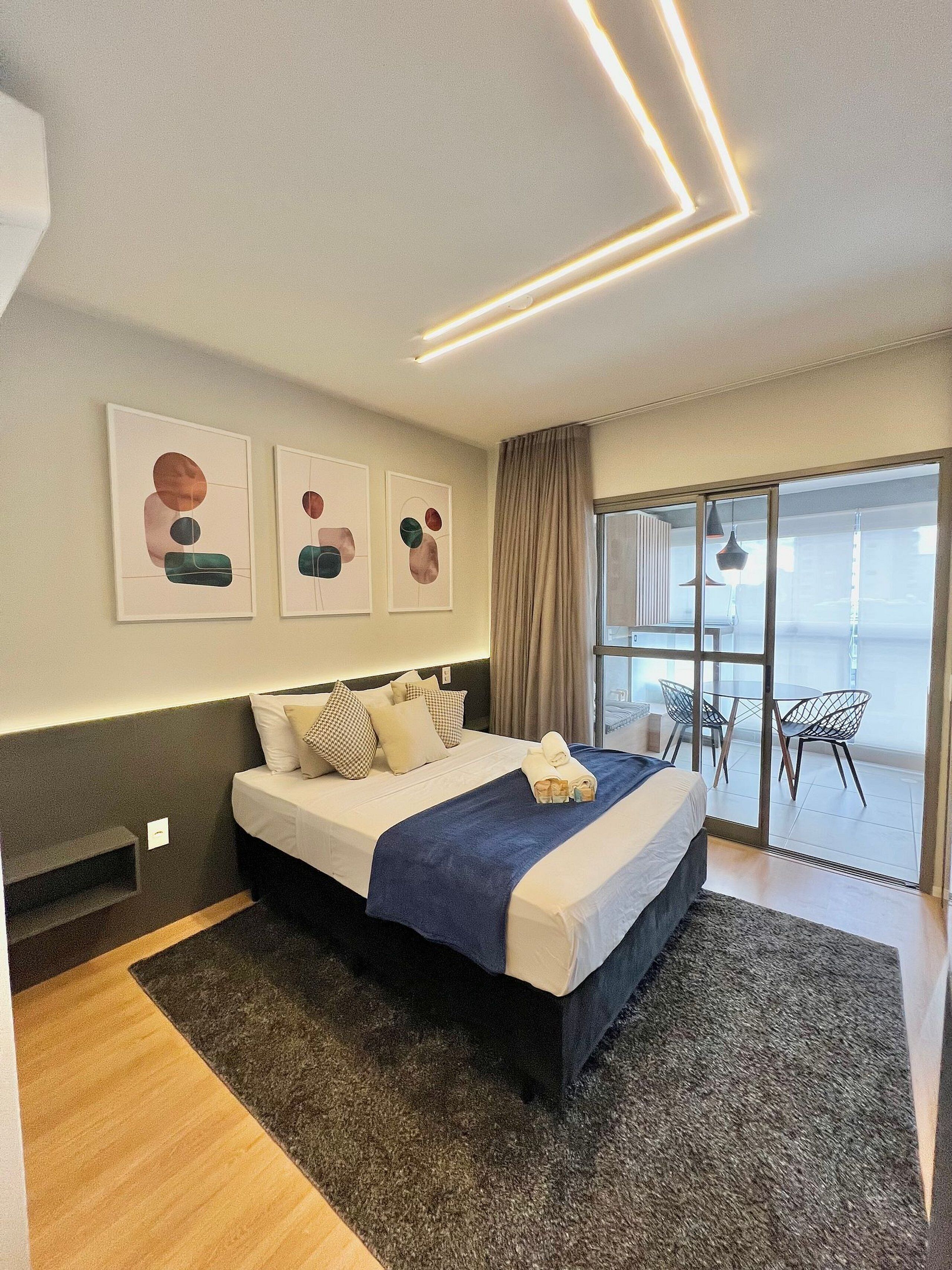 A modern hotel room with a large bed, a view to the outside, and abstract wall art.