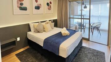A modern hotel room with a large bed, a view to the outside, and abstract wall art.