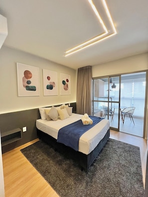 A modern hotel room with a large bed, a view to the outside, and abstract wall art.