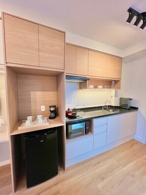 A compact kitchen with wooden cabinets, a built-in dishwasher, a microwave, and a stovetop. - Innvista - AirBrooklin (São Paulo)