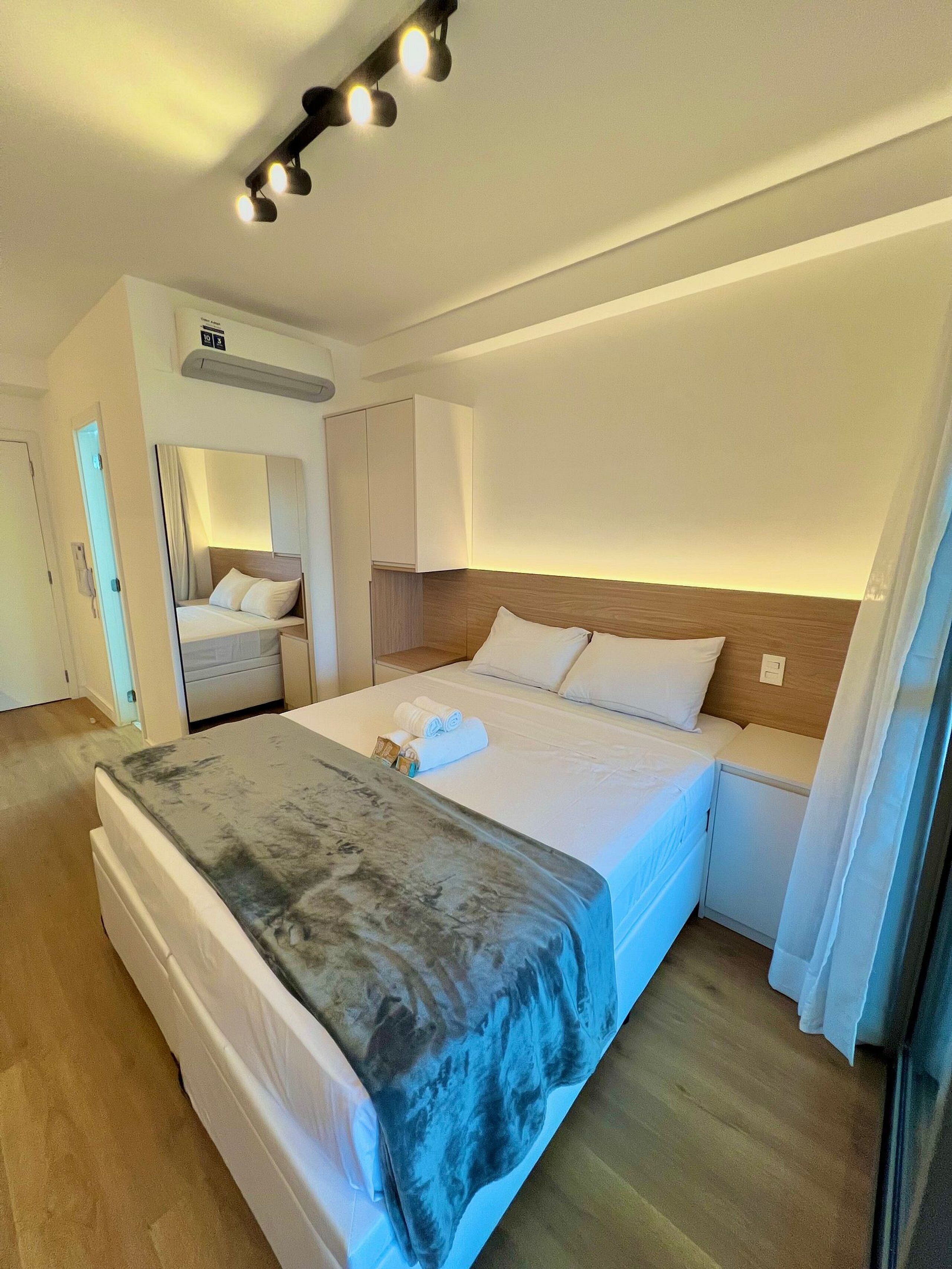 A hotel room with a bed, a bedside table, a mirror, a wardrobe, and a ceiling light fixture.