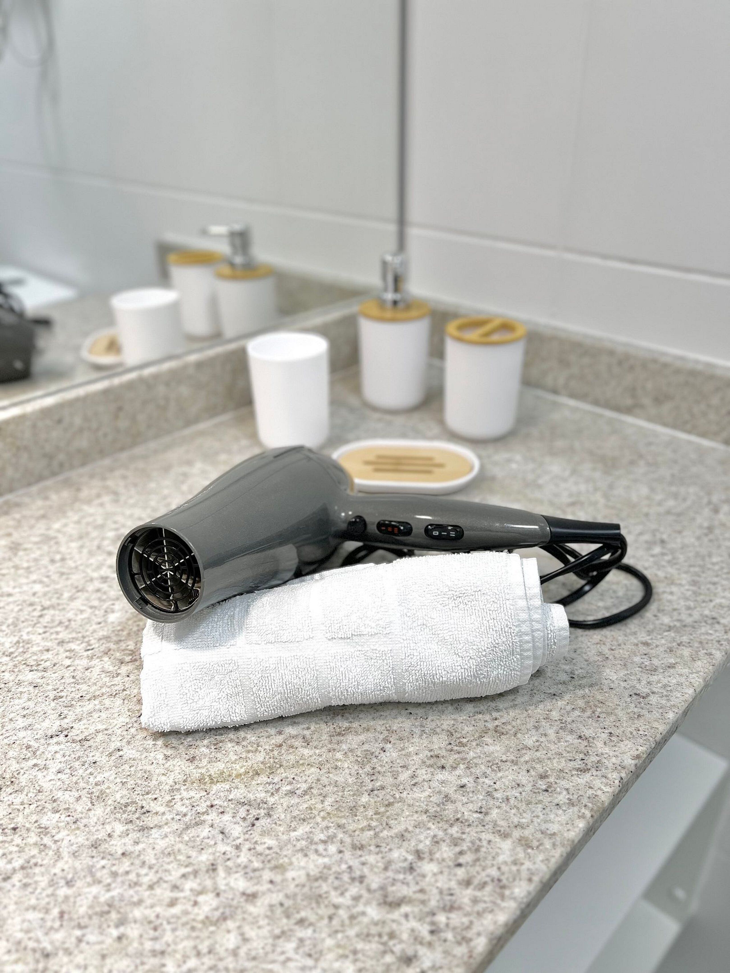 A hair dryer on a countertop with a towel, a mirror, and toiletries in the background.