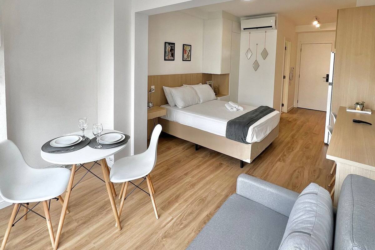 Moderni hotellihuone, jossa on sänky, ruokapöytä tuoleineen, sohva ja pieni keittiönurkkaus.