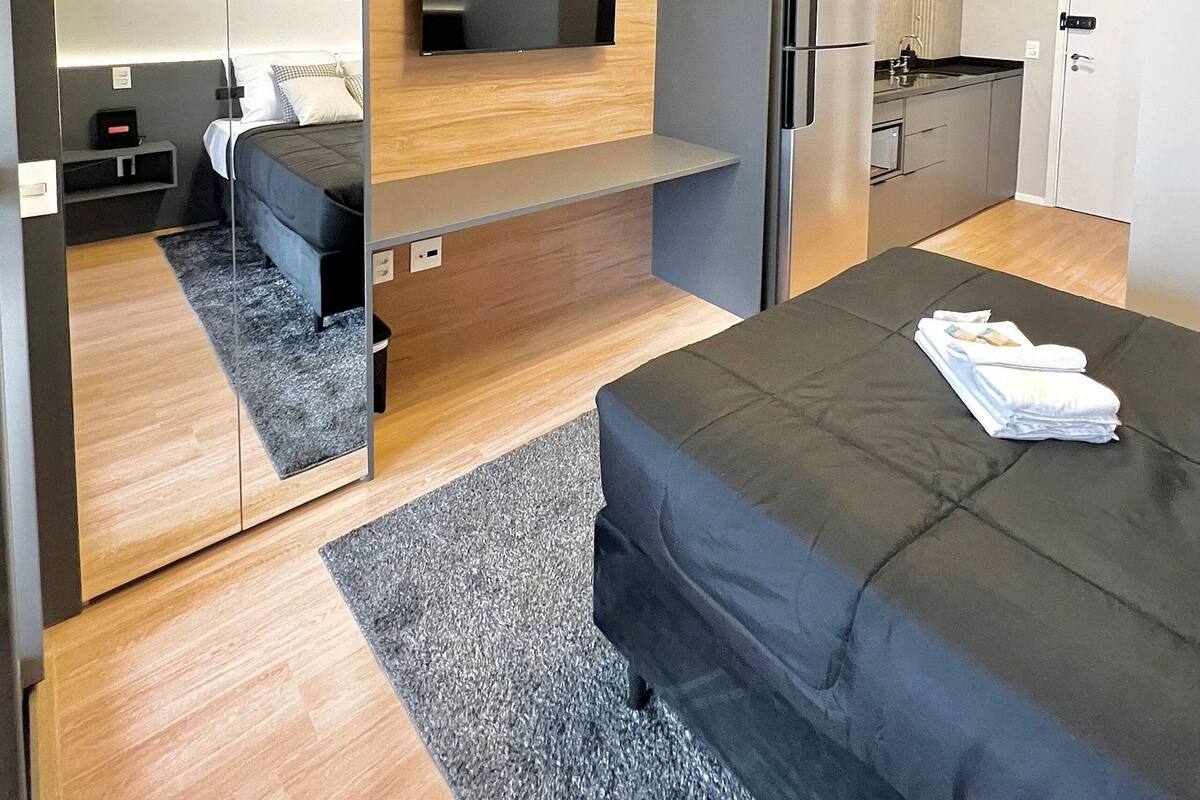 Moderni hotellihuone, jossa on sänky, seinälle asennettu televisio, keittotila ja kylpyhuone.