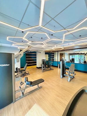 Une salle de sport moderne équipée de matériel d’exercice, dotée d’un plancher en bois et d’un plafond au design géométrique.