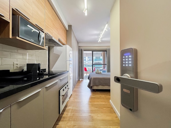 Une cuisine moderne dotée d’appareils électroménagers intégrés, d’un plan de travail en bois et d’un couloir menant à une chambre à coucher avec un lit et une vue sur l’extérieur.