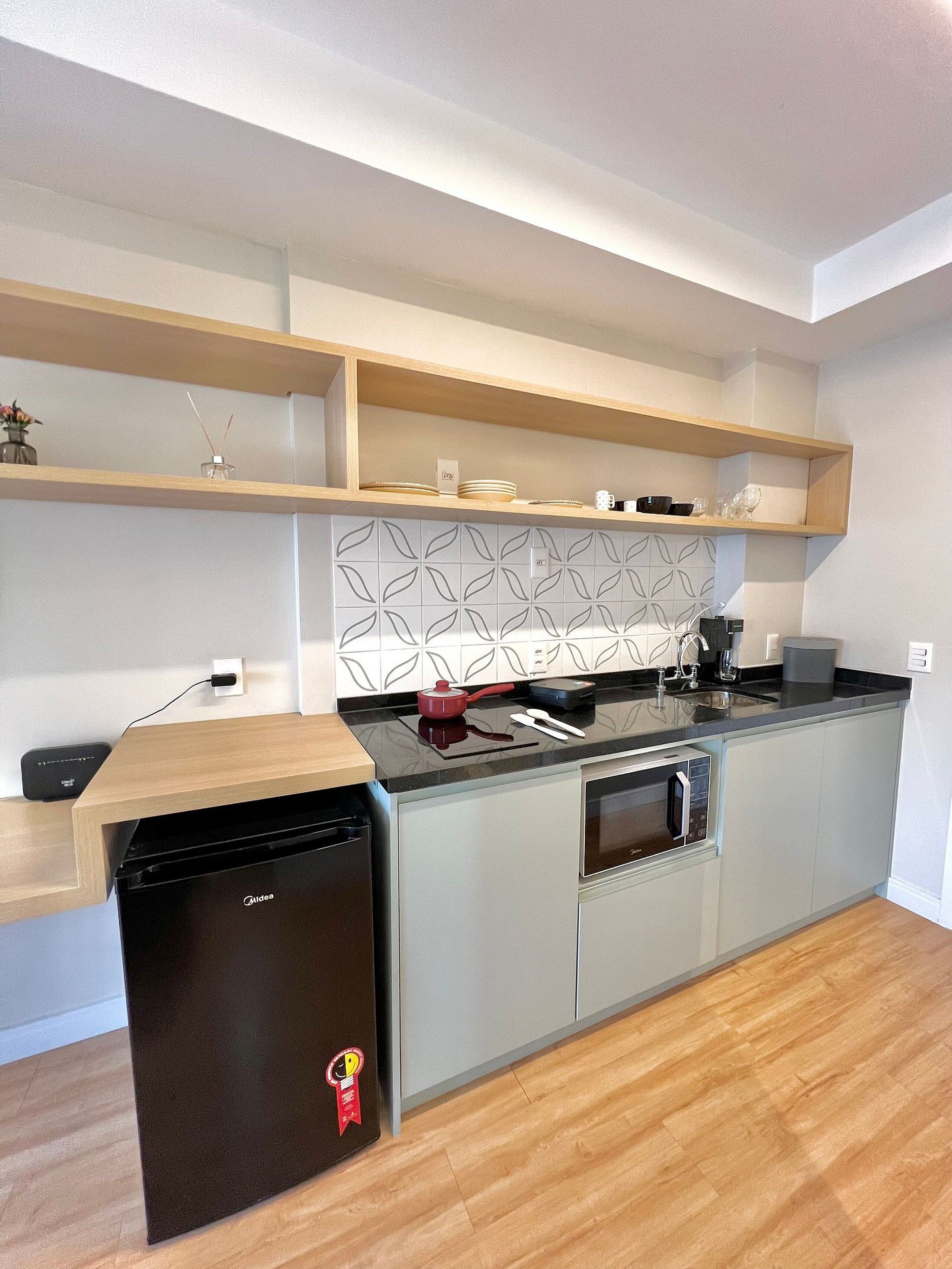 A compact kitchen with a dishwasher, oven, and microwave. There are wooden shelves above the countertop and a patterned backsplash.
