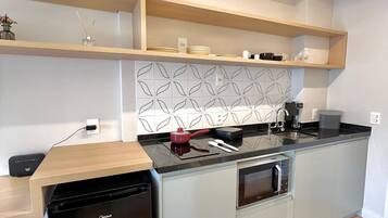 A compact kitchen with a dishwasher, oven, and microwave. There are wooden shelves above the countertop and a patterned backsplash.