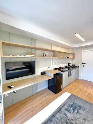 A modern kitchen with built-in appliances, wooden shelves, and a flat-screen TV.