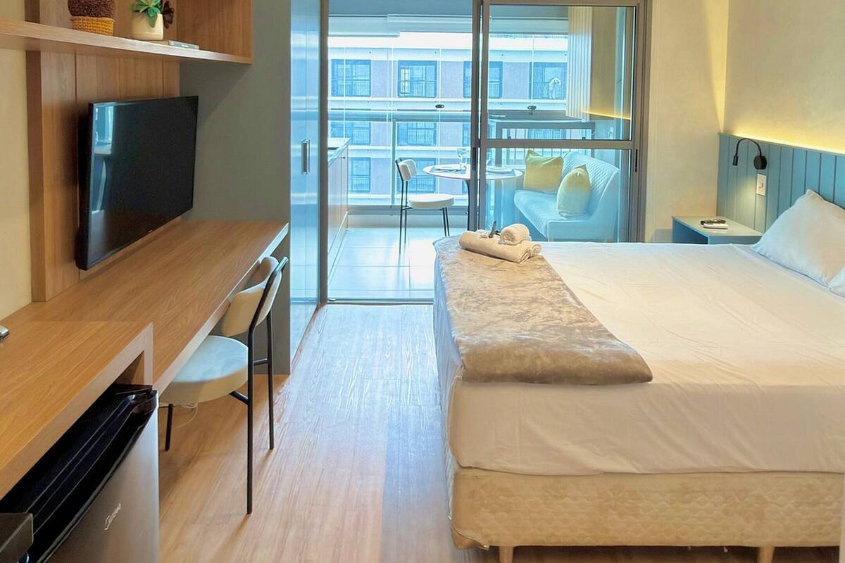 Moderni hotellihuone, jossa on sänky, televisio, työpöytä ja parveke, jolta on näkymä.