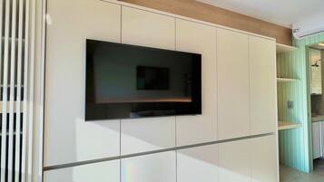 Habitació moderna amb televisió de pantalla plana penjada a la paret, biga de sostre de fusta i terra enrajolada.