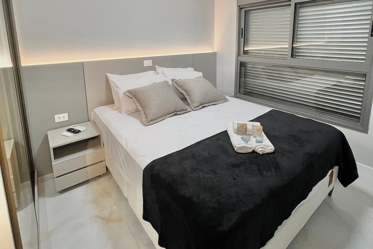 Una habitación de hotel moderna con cama, mesita de noche y ventana con persianas.
