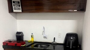 Una cocina compacta con un mueble de madera, un lavamanos, un refrigerador blanco, una cafetera y un letrero sobre el mueble que dice 'NO BAD VIBES'.