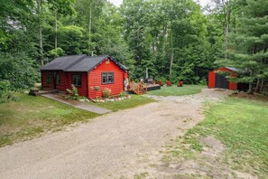 Punainen mökki, jonka edessä on kivituhkapäällysteinen ajotie, ja jonka ympärillä on tiheä metsä.