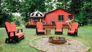 A red cabin with a fire pit and Adirondack chairs in a grassy area. - Cozy Lil Red Cabin; Water Frontage, Dog Friendly! (Ellsworth)