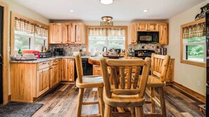 A kitchen with wooden cabinets, a central island, a microwave, and a refrigerator. - Cozy Lil Red Cabin; Water Frontage, Dog Friendly! (Ellsworth)