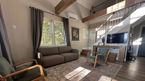 Un salon comprenant un canapé, deux fauteuils, une table basse en bois et une grande fenêtre avec des rideaux.