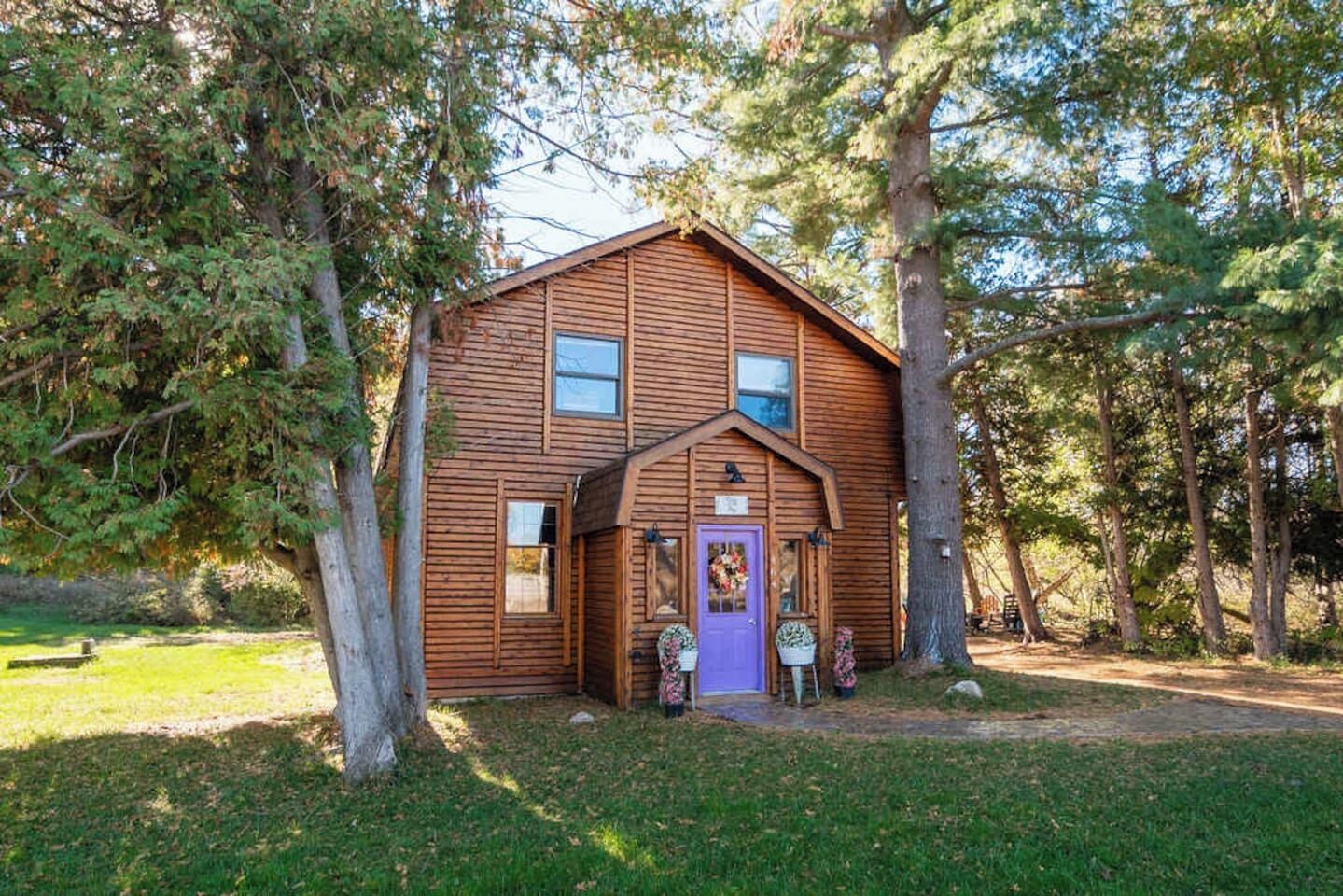 A wooden cabin with a purple door, surrounded by trees.