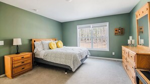 Un dormitorio con cama, mesita de noche, cómoda y ventana con vistas a árboles.