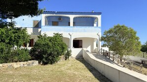 Un bâtiment à deux étages avec une façade bleue, un chemin de pierre menant à l’entrée et une clôture en bois le long du côté.