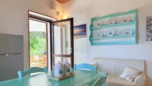 Une pièce avec une table de couleur turquoise, un canapé blanc et une étagère murale ornée d’assiettes décoratives.