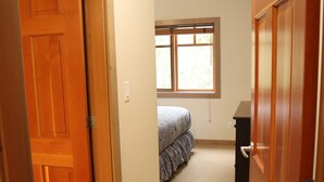 A narrow hallway with wooden doors on both sides, leading to a bedroom with a bed and a window.