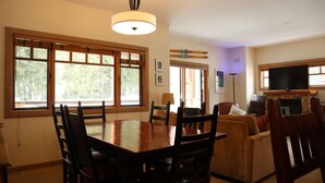 A dining area with a large wooden table and chairs, a sofa, and a fireplace with a TV.