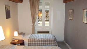 Une chambre avec deux lits, une fenêtre avec des rideaux, une lampe de chevet et un tableau encadré au mur.