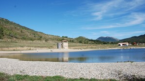 Un cadre paisible au bord d’un lac, avec une petite construction en forme de tour située près du rivage, entourée de collines et d’une végétation clairsemée.