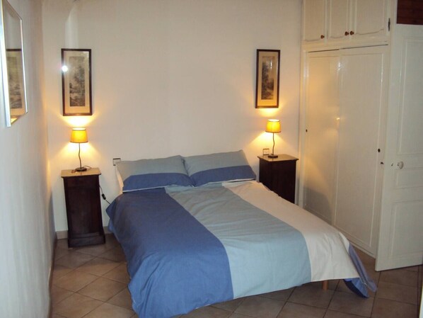 A bedroom with a bed, two bedside tables with lamps, a wardrobe, and two framed pictures on the wall.