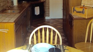 Une cuisine avec des meubles de rangement en bois, un pare-feu en carrelage, un luminaire suspendu et un panier en osier posé sur une table.