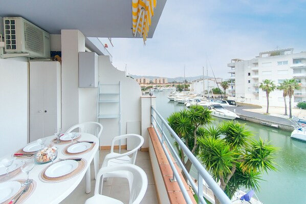 A balcony with a dining setup overlooking a marina with boats and palm trees.