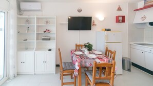 Een eethoek met een tafel voor vier personen, omringd door houten stoelen. Een televisie is aan de muur boven de tafel bevestigd.