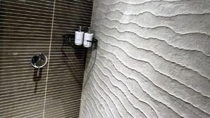 A bathroom with a textured wall, a shower area with a handheld showerhead, and a towel rack with two towels. - Lovely 2-Bedroom Apartment in Cinta Costera (Panamá)