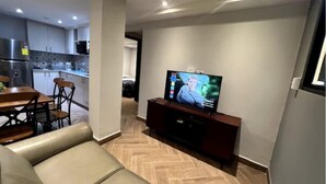 A modern living room with a sofa, TV, and a kitchen in the background. - Lovely 2-Bedroom Apartment in Cinta Costera (Panamá)