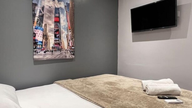 A hotel room with a bed, a TV mounted on the wall, and a cityscape painting on the wall. - Lovely 2-Bedroom Apartment in Cinta Costera (Panamá)