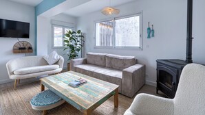 Ein gemütliches Wohnzimmer mit Sofa, Sessel und Couchtisch, inklusive Kamin und großem Fenster.