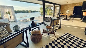 A modern living room with a large window overlooking a lake, furnished with a sofa, chairs, and a dining table. - WTF  HOUSE (Beograd)