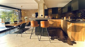 A modern kitchen with a central island, bar stools, and a dining area with a table and chairs. - WTF  HOUSE (Beograd)