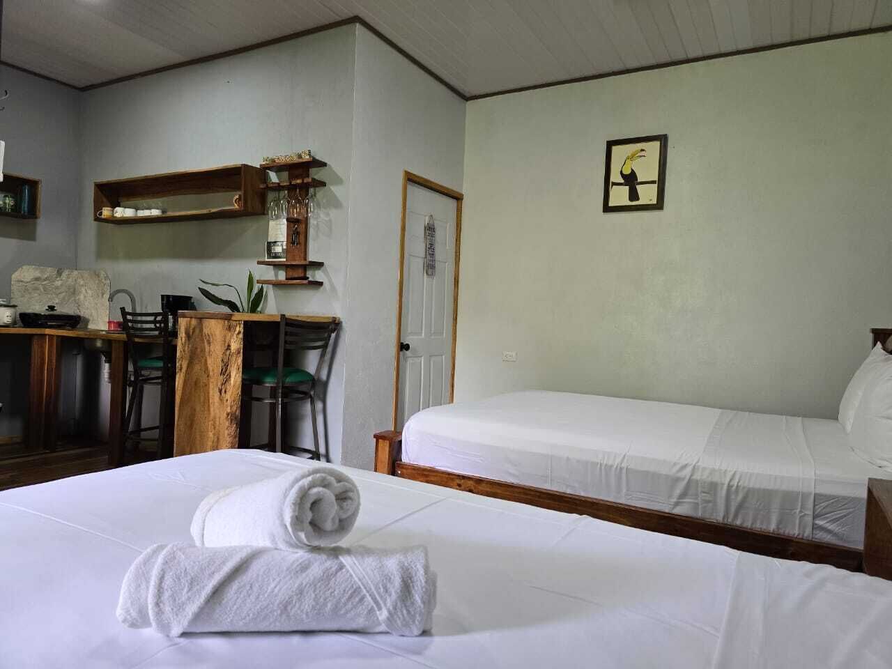 Habitación de hotel con dos camas, un escritorio con sillas, una mesa de madera y un cuadro en la pared.
