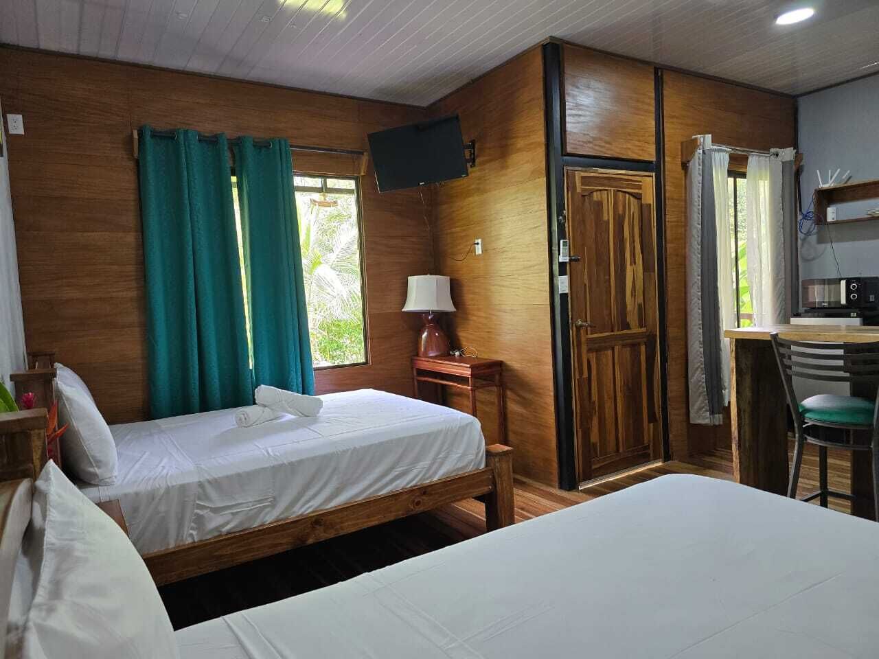 Una habitación con dos camas, un escritorio, una silla, un televisor y una ventana con cortinas.