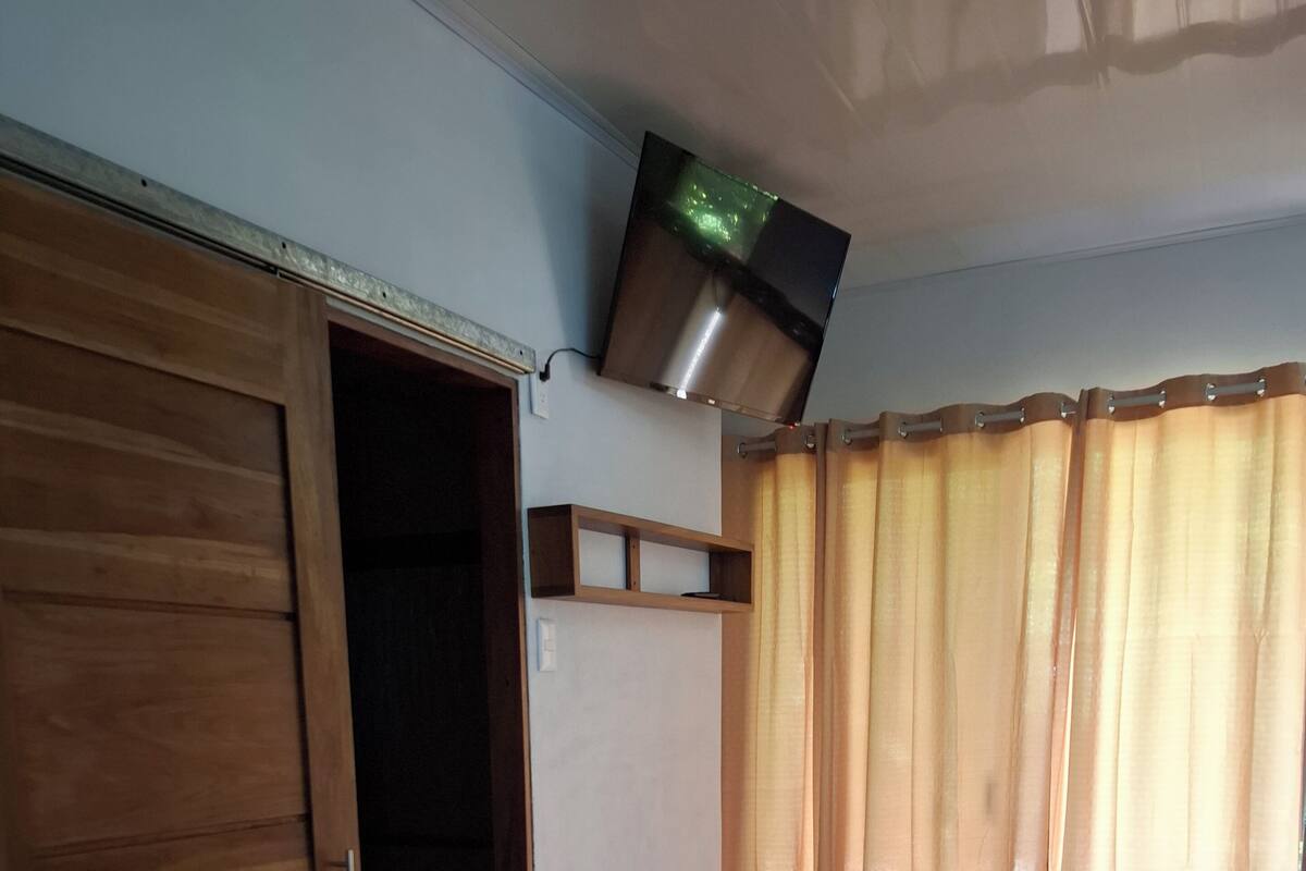 Een kamer met een houten garderobe, een flatscreen televisie aan de muur en een raam met gordijnen.