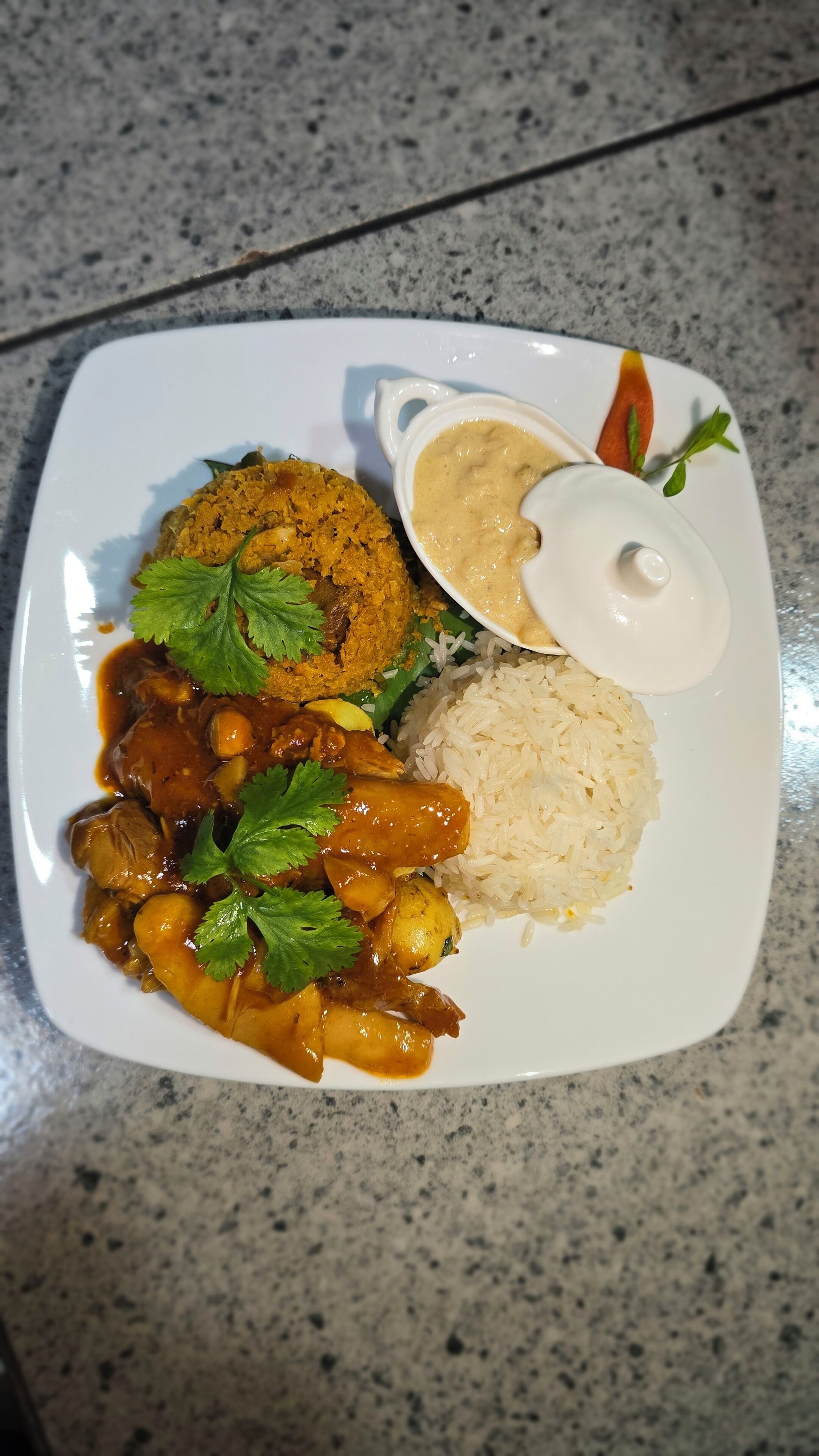 Ein Teller mit Reis, einem Currygericht und einer Soße auf einer Granitabdeckung.