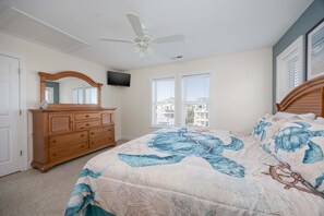 Une chambre avec un lit, une commode, un ventilateur de plafond et un téléviseur fixé au mur.