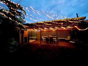 Relax in the covered patio area with tables and chairs, surrounded by a fence and a door leading to the interior.
