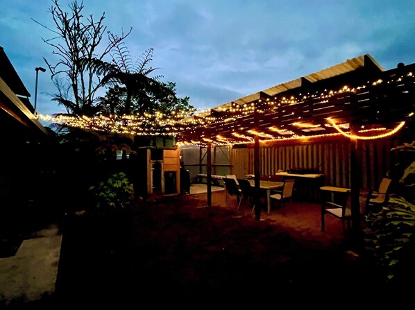 Relax under a shaded pergola surrounded by lush greenery and string lights.
